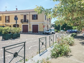 A street view with a yellow building, closed shutters, and a cobblestone road. - EnDi (Asti)