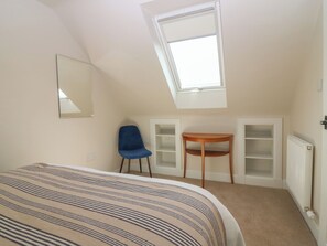 Un dormitorio con techo inclinado, una cama, una silla, una mesita y estanterías empotradas.