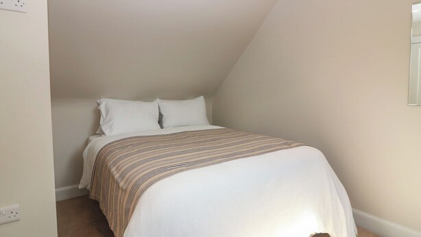 A bedroom with a bed, white walls, and a sloped ceiling. - Keepers Cottage (Haddington)