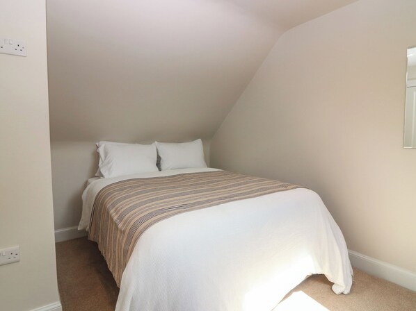 A bedroom with a bed, white walls, and a sloped ceiling.
