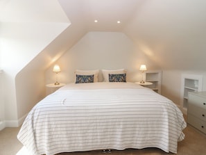 A bedroom with a sloped ceiling, a bed with striped bedding, two bedside lamps, and a white nightstand. - Keepers Cottage (Haddington)