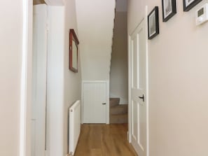 A narrow hallway with a wooden floor, white walls, and a white door at the end.