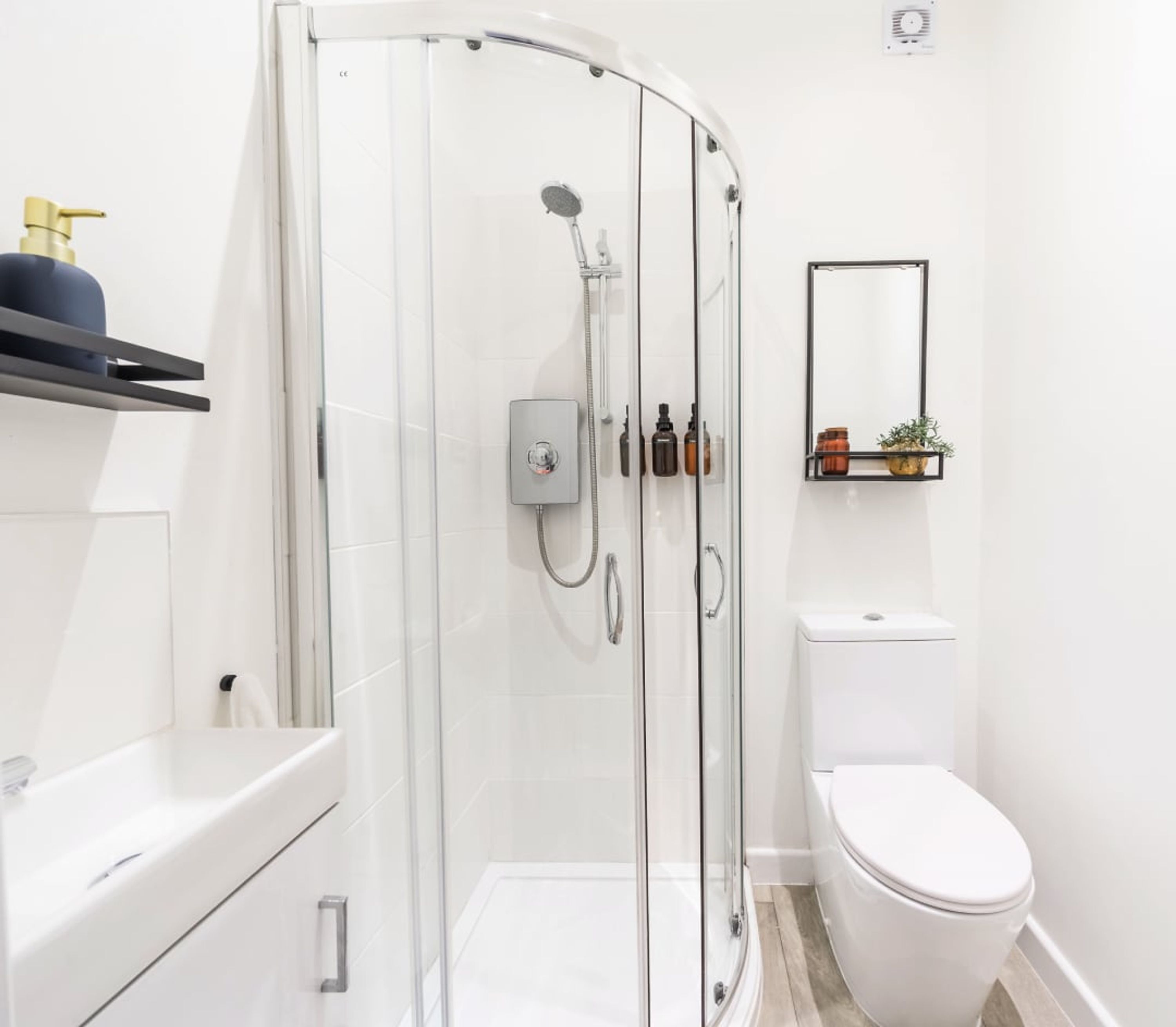 A modern bathroom with a glass-enclosed shower, a white toilet, and a shelf with toiletries.