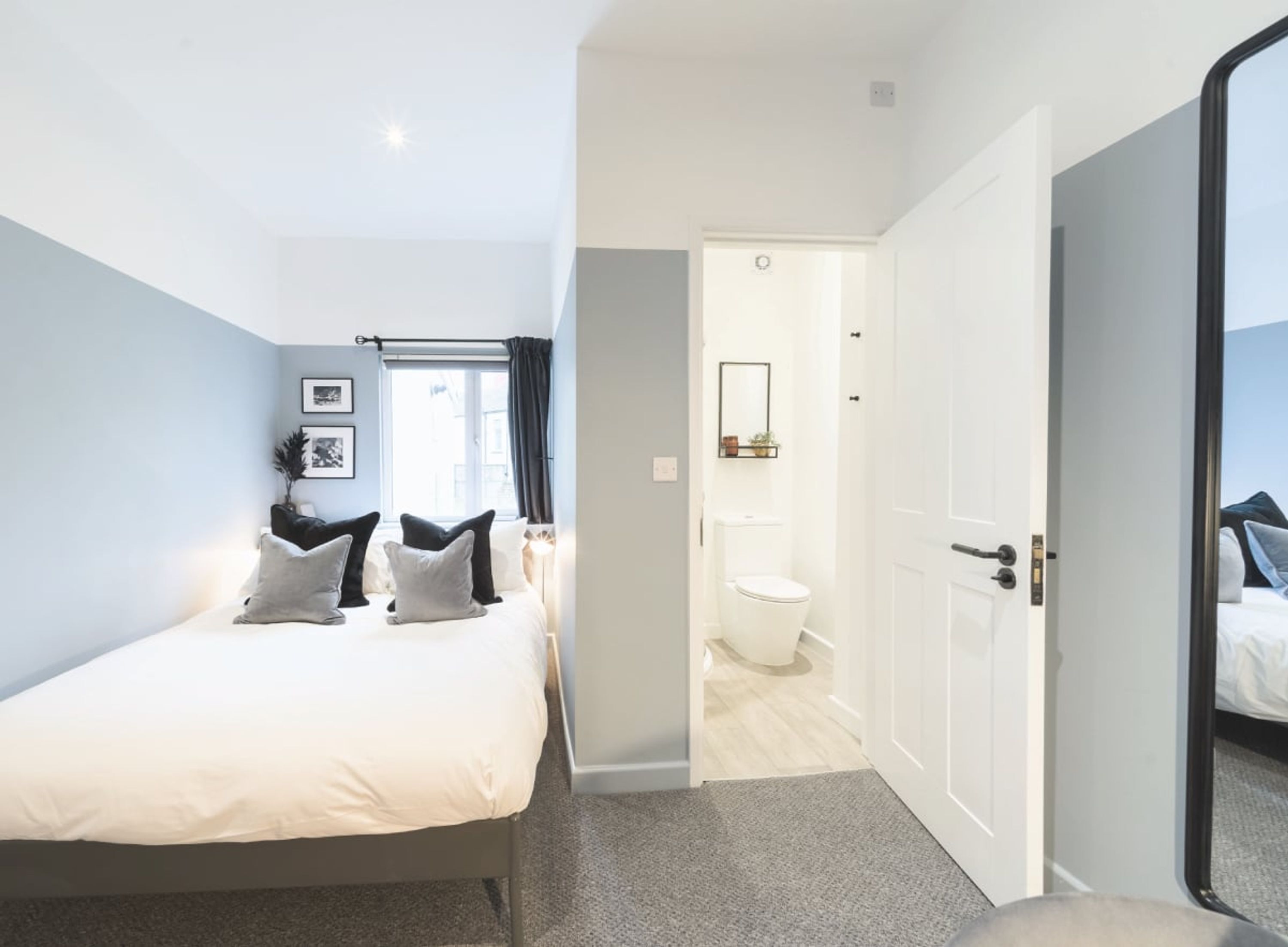 Une chambre à coucher avec un lit, des oreillers, une fenêtre et une porte donnant sur une salle de bain.