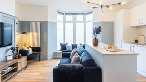 Una sala de estar moderna con sofá, televisor, lámpara y un ventanal grande.