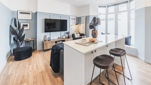 Una cocina moderna con una isla central, taburetes de bar, un televisor de pantalla plana y un ventanal grande.
