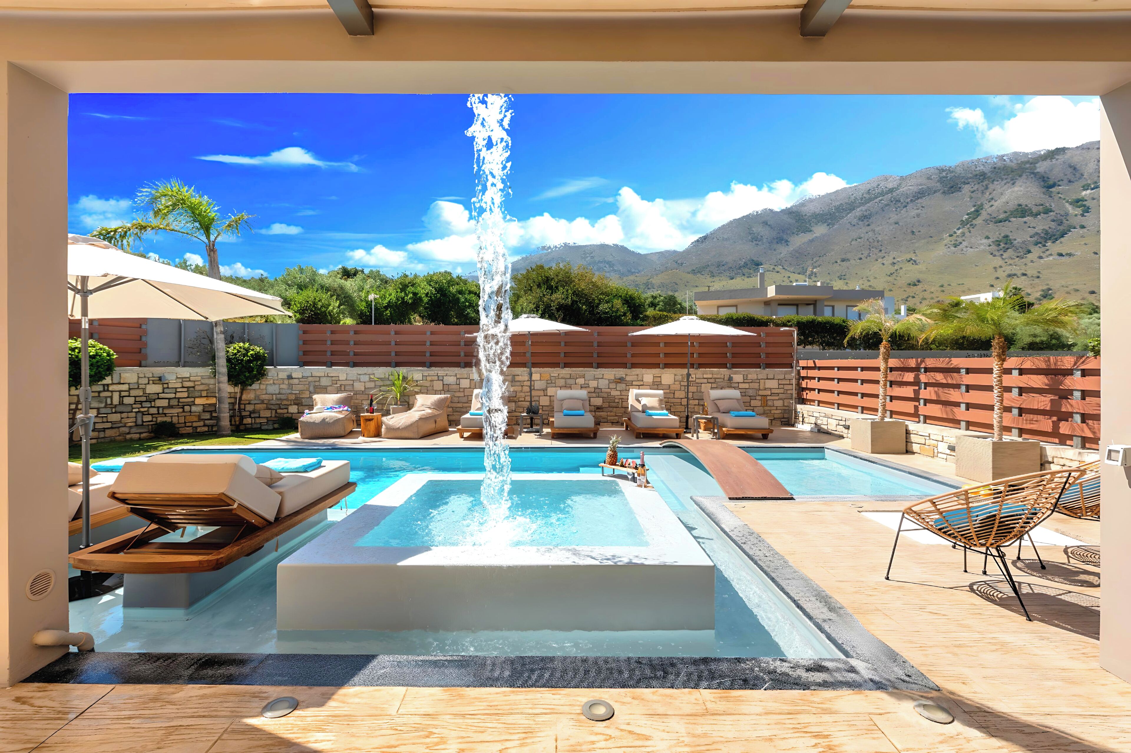 A pool area with a central water feature, lounge chairs, and a view of mountains.
