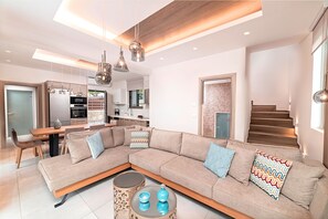 Ein modernes Wohnzimmer mit einer Eckcouch, einem Esstisch und einer Küche im Hintergrund.