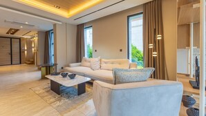 A modern living room with a sofa, coffee table, and a view of greenery outside.