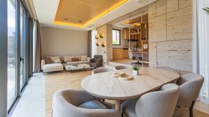 A modern living room with a round dining table, a sofa set, and a kitchen area with built-in shelving.