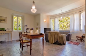 A spacious living area with a dining table, sofa, and TV. Large windows provide natural light and views of greenery. - Casa Bedella · Private villa with garden (Lanzo D'intelvi)