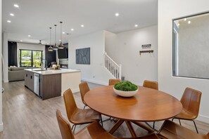 Eine moderne Küche mit einer zentralen Kochinsel, Essbereich mit rundem Tisch und Stühlen sowie eine Treppe, die in ein Obergeschoss führt.