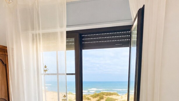 A bedroom with a bed, a yellow pillow, and a view of the beach through an open door. - One-bedroom apartment facing the ocean (Leiria)