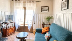 A cozy living room with a wooden ceiling, a sofa with colorful cushions, a small round table, and a television on a wooden cabinet. - One-bedroom apartment facing the ocean (Leiria)