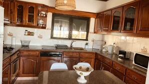 A kitchen with wooden cabinets, a dining table with chairs, a hanging light fixture, and a window. - One-bedroom apartment facing the ocean (Leiria)