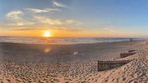 A beach with a wooden boardwalk leading to the water, a lifeguard stand, and a clear sky. - One-bedroom apartment facing the ocean (Leiria)