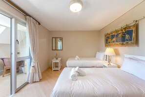 Quarto de hotel com duas camas, uma porta de vidro deslizante, uma mesa pequena, uma luminária e um espelho fixado na parede.