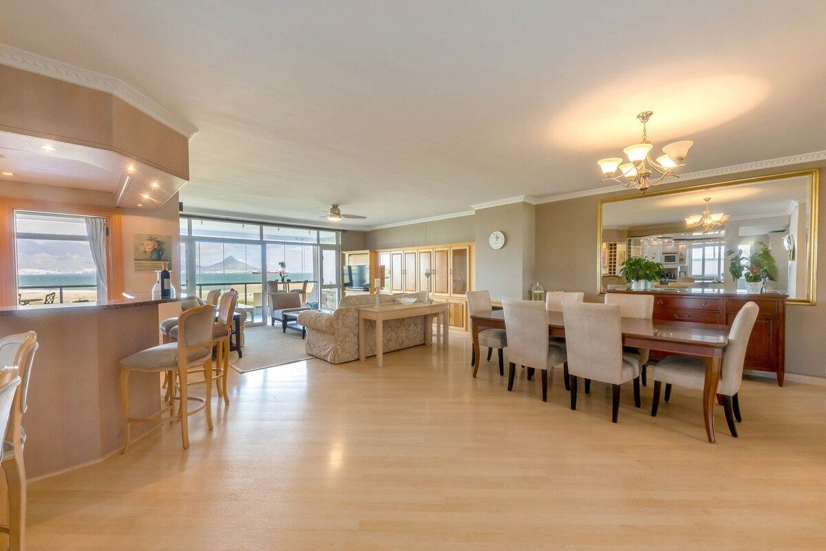 A spacious living area with a dining table, chairs, and a bar area with stools.