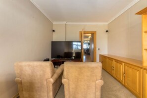 Una sala de estar con dos sillones color beige, un televisor y un aparador de madera.