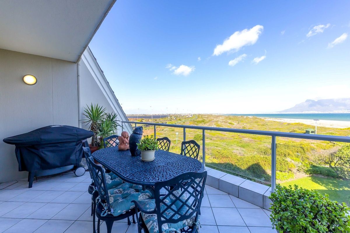 Un balcon avec une table et des chaises, un barbecue et une vue sur le paysage.