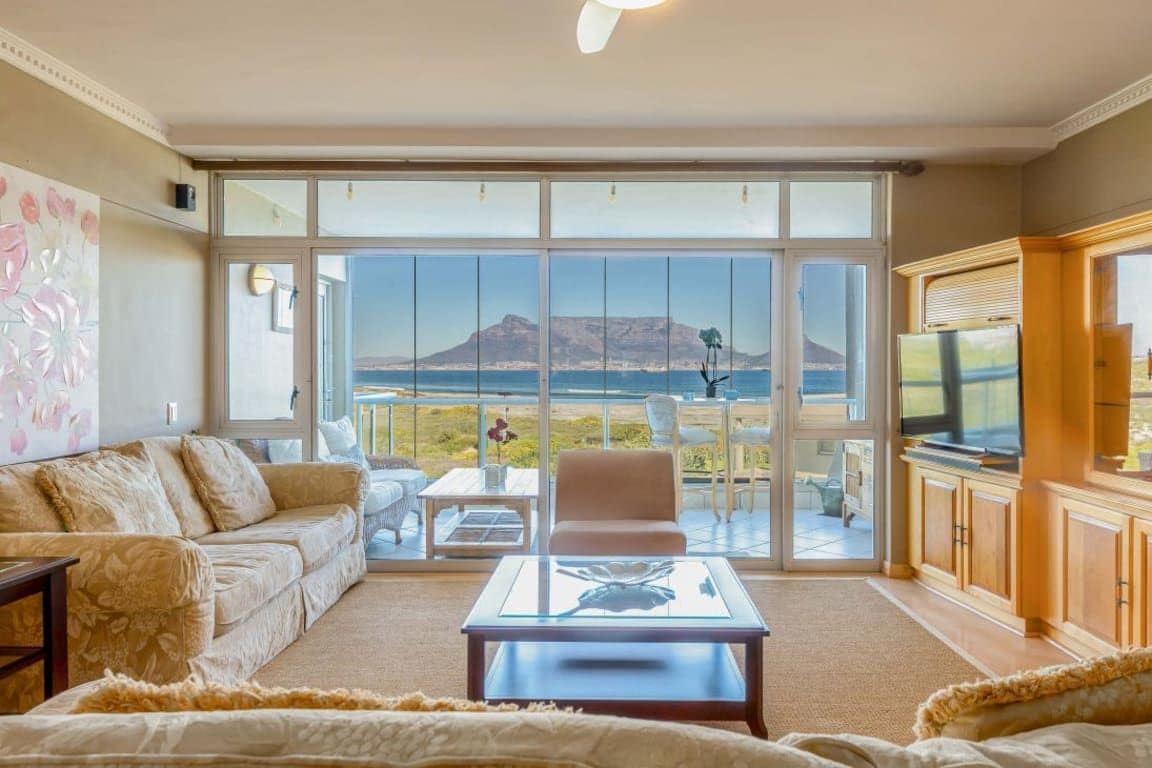 A living room with a sofa, coffee table, and a television. There is a large sliding glass door leading to a balcony with a view of a mountain.