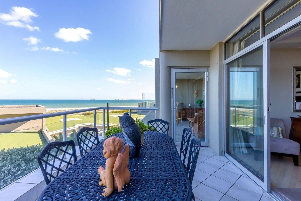A balcony with a view of the beach, a table with chairs, and a sofa.