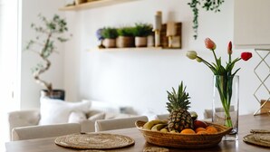 A dining table with a fruit bowl, a vase with flowers, and a clear glass vase.