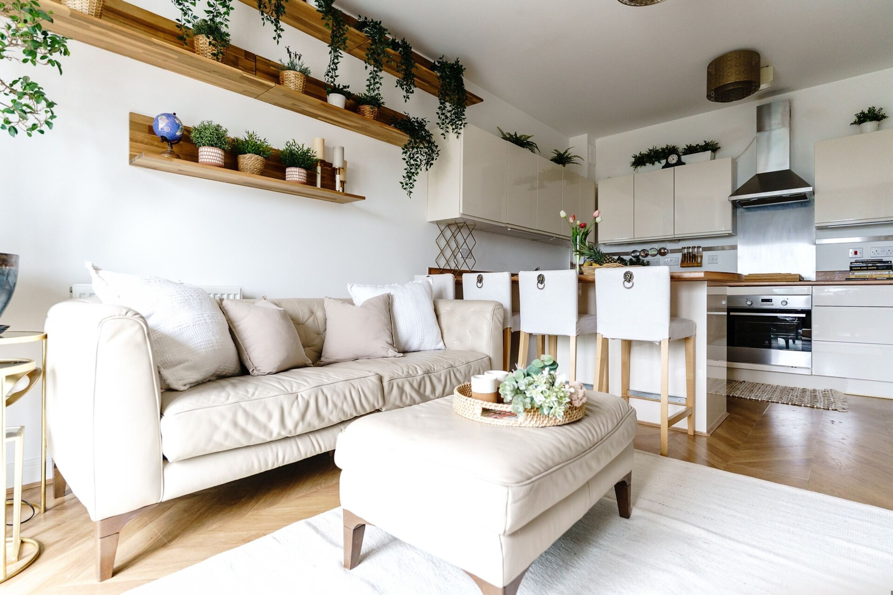 A modern living room with a sofa, ottoman, and a kitchen area with cabinets and a stove.