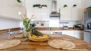 A kitchen with a wooden countertop, a fruit bowl, a vase with flowers, and a clock on the wall.