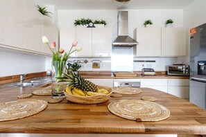 Eine Küche mit einer Holzausziehtheke, einer Obstschale, einer Blumenvase und einer Uhr an der Wand.