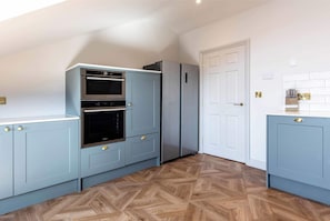 A kitchen with light blue cabinets, a double oven, a refrigerator, and a wooden herringbone floor. - Luxury Penthouse in the City (Nottingham)