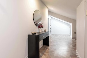 A hallway with a dark console table, a round mirror, and a vase with red flowers. - Luxury Penthouse in the City (Nottingham)