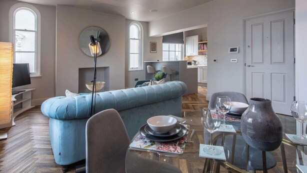 A modern living room with a blue sofa, a dining table set with plates and glasses, and a large vase. - Central, Secure Parking and High-end (Nottingham)