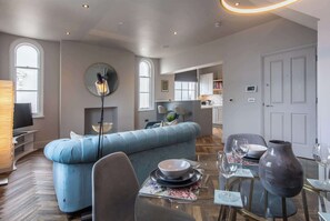 Uma sala de estar moderna com um sofá azul, uma mesa de jantar posta com pratos e copos, e um vaso grande.