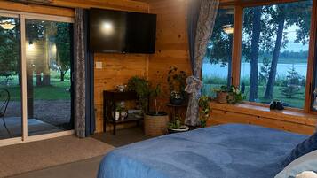 Habitación de cabaña de madera con cama, televisor, escritorio y vistas al exterior.