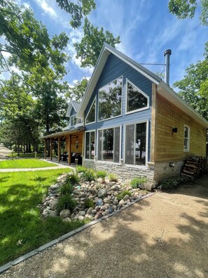 Ein zweigeschossiges Haus mit überdachter Veranda, einem Steinfundament und einem gepflegten Rasen.