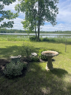 A garden with a birdbath, a statue, and a lake in the background. - Adorable Lakeside Cabin w/ Private Sandy Beach to Enjoy the Sunrise (Menahga)