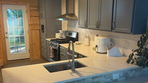 Une cuisine dotée d’un grand îlot central, d’appareils électroménagers en acier inoxydable et offrant une vue sur l’extérieur grâce à une porte vitrée.