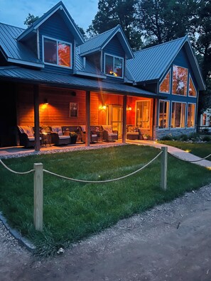 A two-story wooden cabin with a covered porch, outdoor seating, and a stone foundation. - Adorable Lakeside Cabin w/ Private Sandy Beach to Enjoy the Sunrise (Menahga)