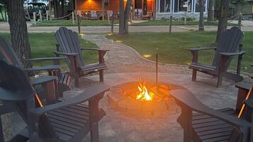 A fire pit with Adirondack chairs, a building with a metal roof, and a gravel path.