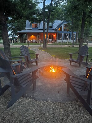 Ein Lagerfeuer mit Adirondack-Stühlen, ein Gebäude mit Metalldach und ein Kiesweg.
