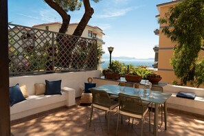 An outdoor patio with a table and chairs, a sofa with cushions, potted plants, and a view of the sea. - Via Francesco Petrarca 93 (Naples)