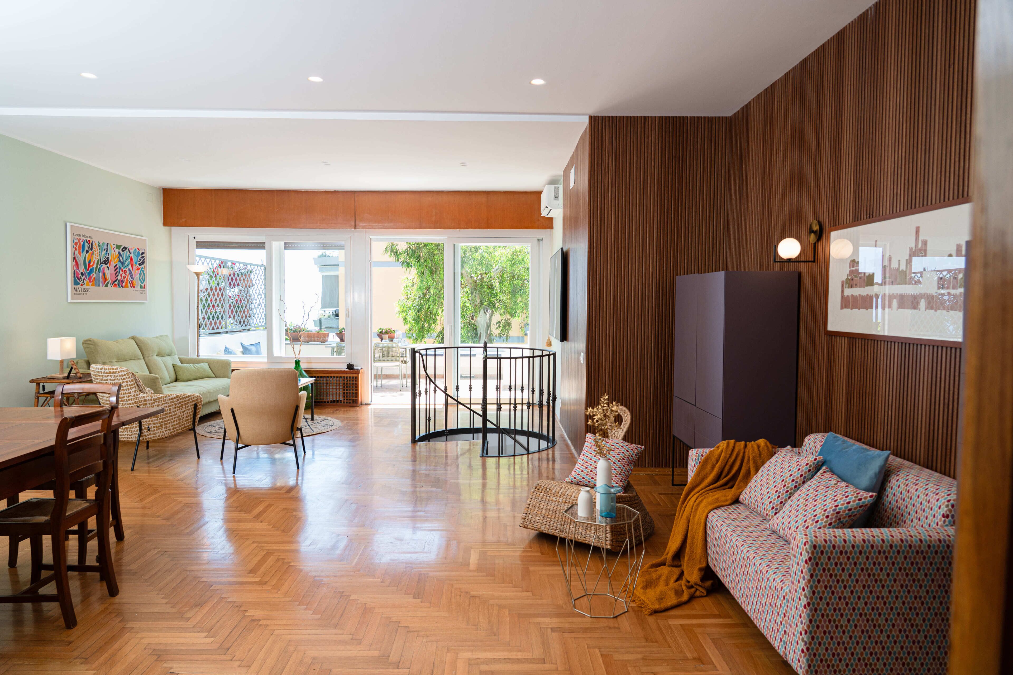Een ruime woonkamer met houten vloer, een bank, een eettafel en een trap.