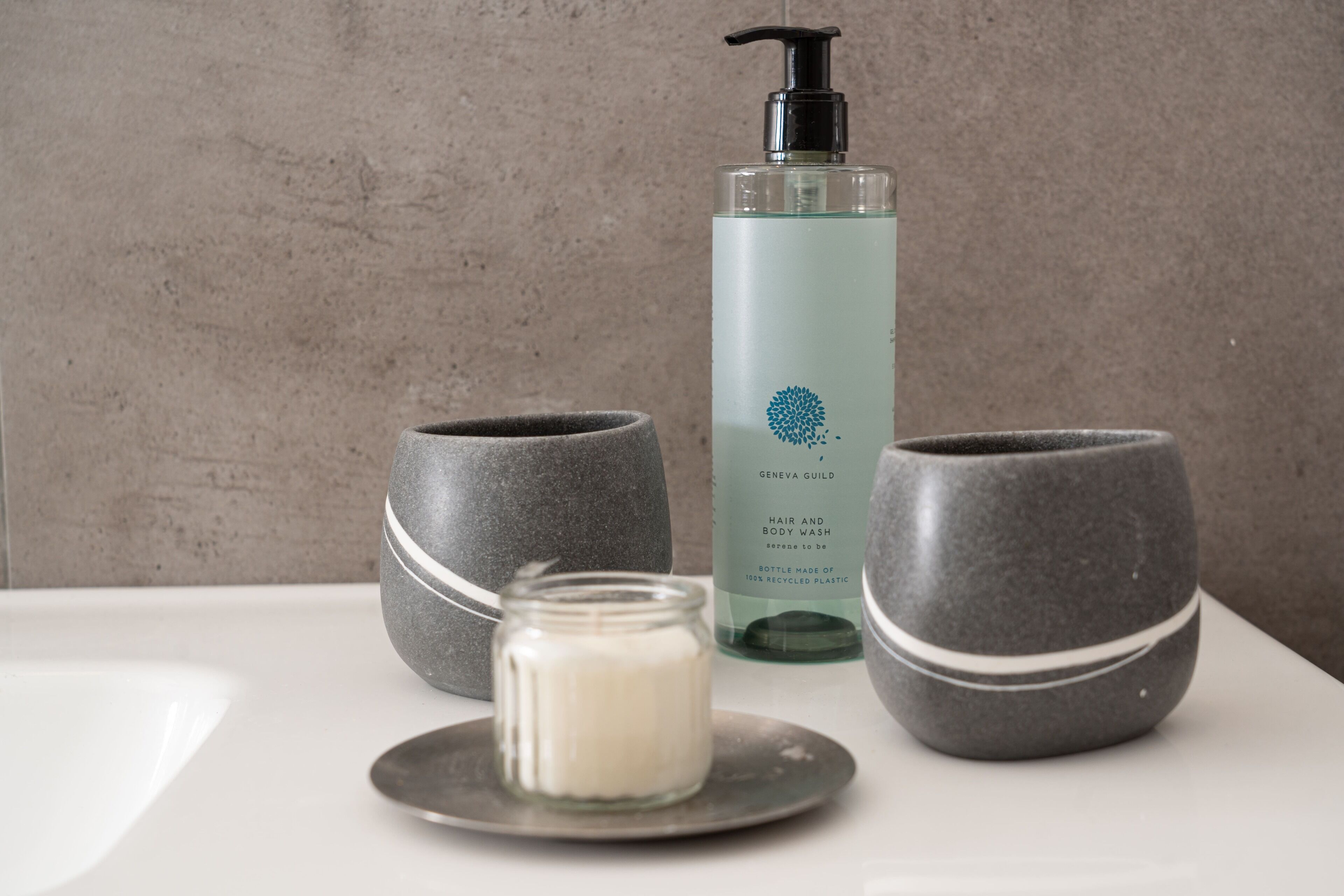 A bathroom with a white sink, two grey ceramic bowls, a glass jar with a white substance, and a bottle of liquid soap.