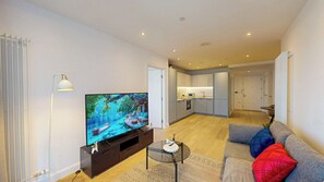 Ein modernes Wohnzimmer mit Flachbildfernseher, einer Couch, einem Couchtisch und einer Küche im Hintergrund.