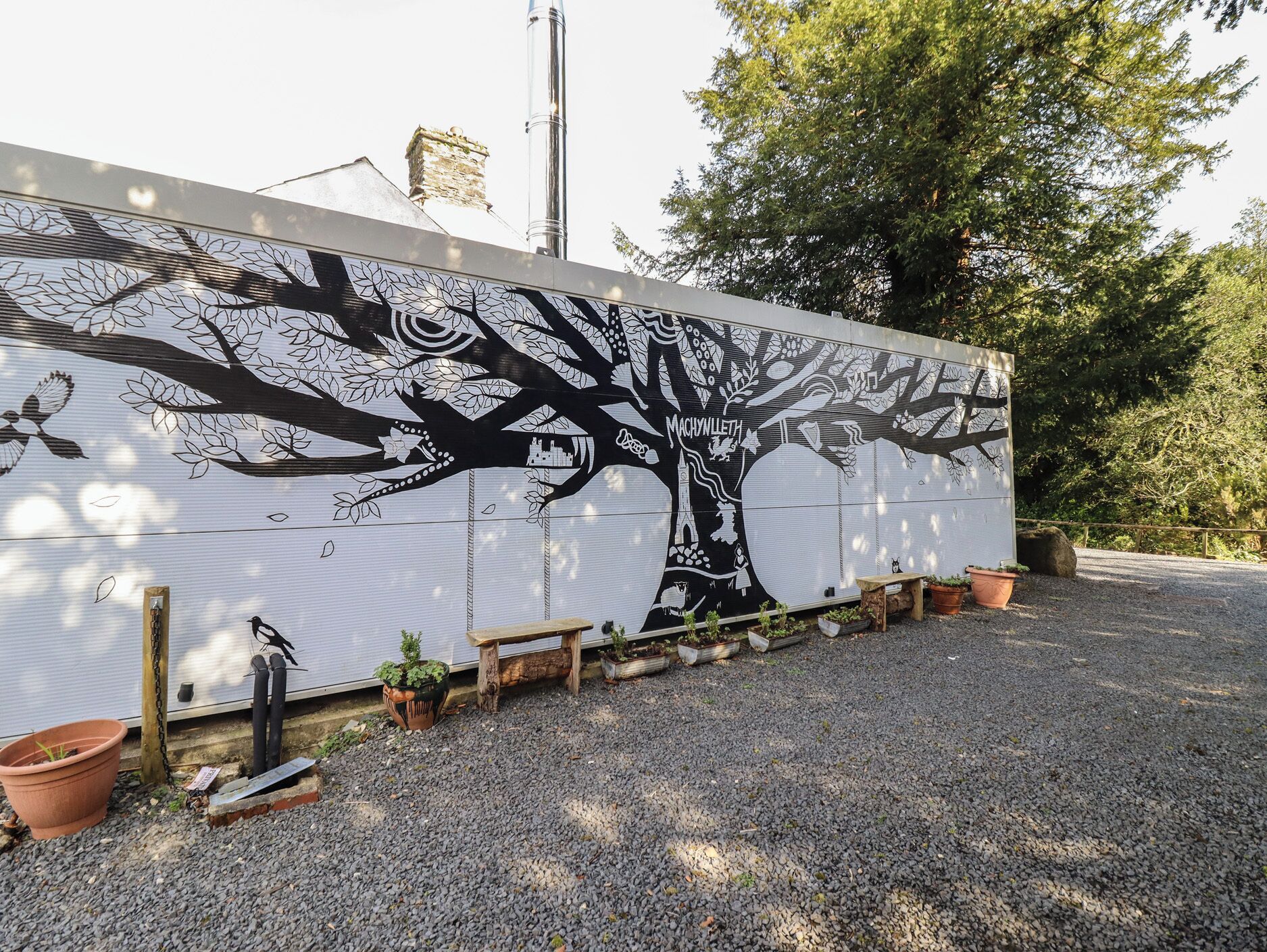 A large wall mural with a tree and bird designs, surrounded by gravel and potted plants.