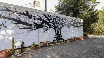 A large wall mural with a tree and bird designs, surrounded by gravel and potted plants.