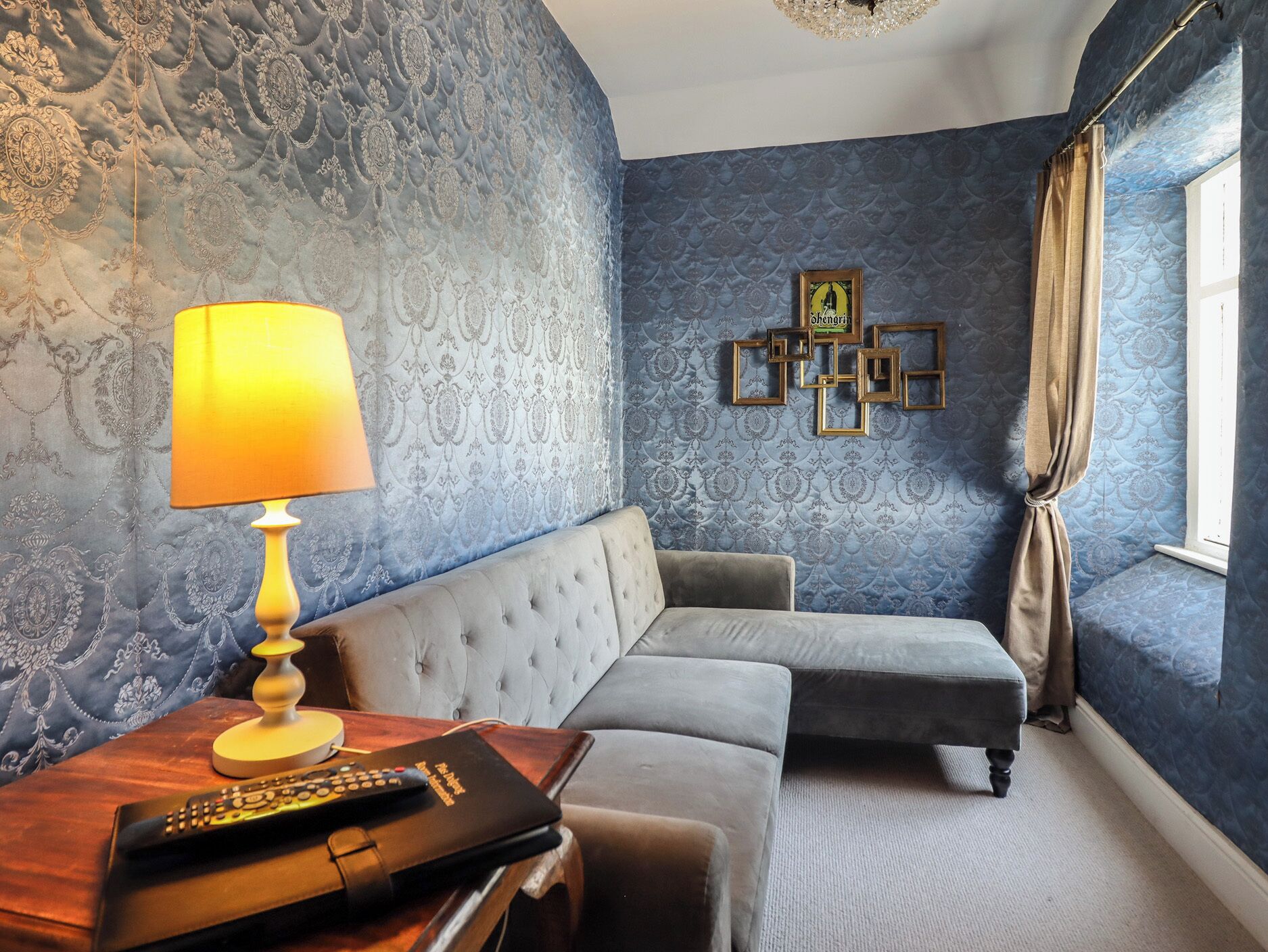 A room with a tufted sofa, a lamp, a remote control, and a wall with a patterned design.