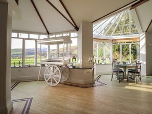 A conservatory with a wooden floor, a white carriage, and a dining table with chairs. - Plas Dolguog (Machynlleth)