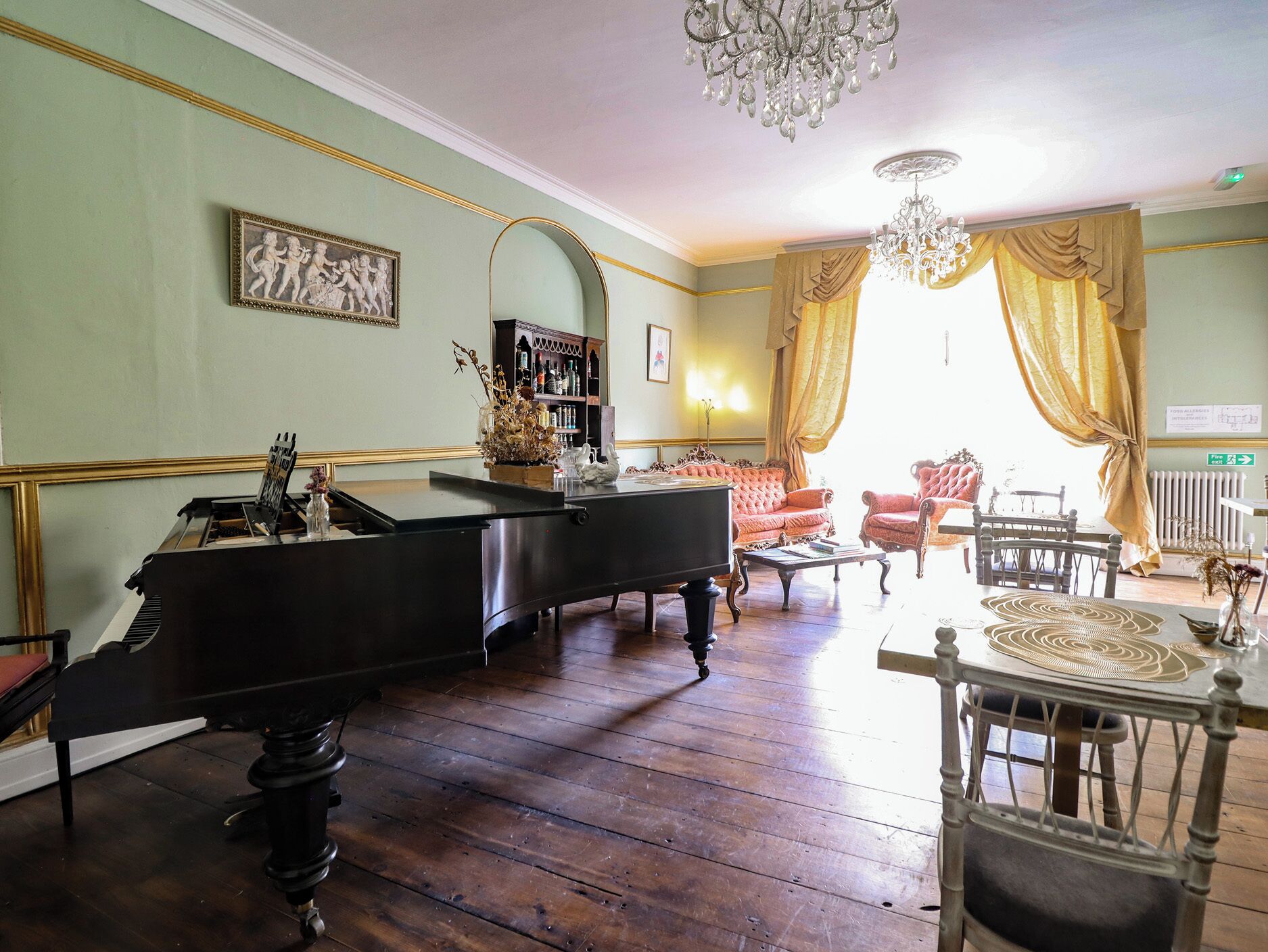 A grand piano, a red sofa, a dining table with chairs, and a chandelier in a room with wooden floors and green walls.